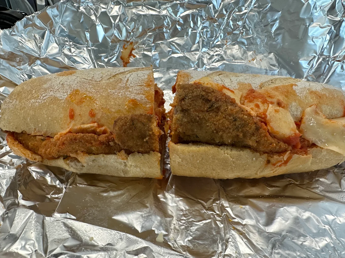 A breaded cutlet sandwich with cheese and tomato sauce wrapped in takeaway foil